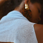 A close-up shot of a model from behind wearing a light blue open-knit sleeveless top and large gold hoop earrings.