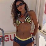 Model wearing a navy blue bikini with a yellow and navy checkerboard pattern on the top and a solid yellow waistband on the bottom.