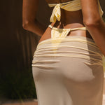 Model wearing a yellow bikini and matching sheer maxi skirt against a blurred background