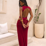 Back of model wearing a cherry Rogue Season one-piece swimsuit with side cut-out and matching sheer skirt, standing indoors in a neutral setting.