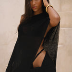 Model wearing a black sarong and black matching cape, posing in front of a neutral background