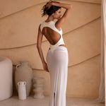 Back shot of model wearing an ivory bodysuit with a matching sheer maxi skirt with a fitted silhouette, standing indoors against a neutral-toned wall with minimal decor.