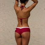 Back image of model wearing a two-piece bikini on a sandy beach. The bottoms are cherry with a light pink waistband and a small pink logo on the side.