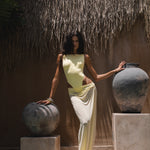 Model in a yellow swimsuit with a matching sheer maxi skirt, standing between two large pots in a tropical setting