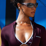 Model wearing a burgundy short-sleeve athletic zip-front top with white trim and a front zipper, shown in a close-up outdoor shot against a blue background.