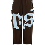 Dark brown balloon pants featuring a large light blue gothic-style 'rs' graphic on the front, with brown drawstrings at the sides and hems, shown against a plain white background.